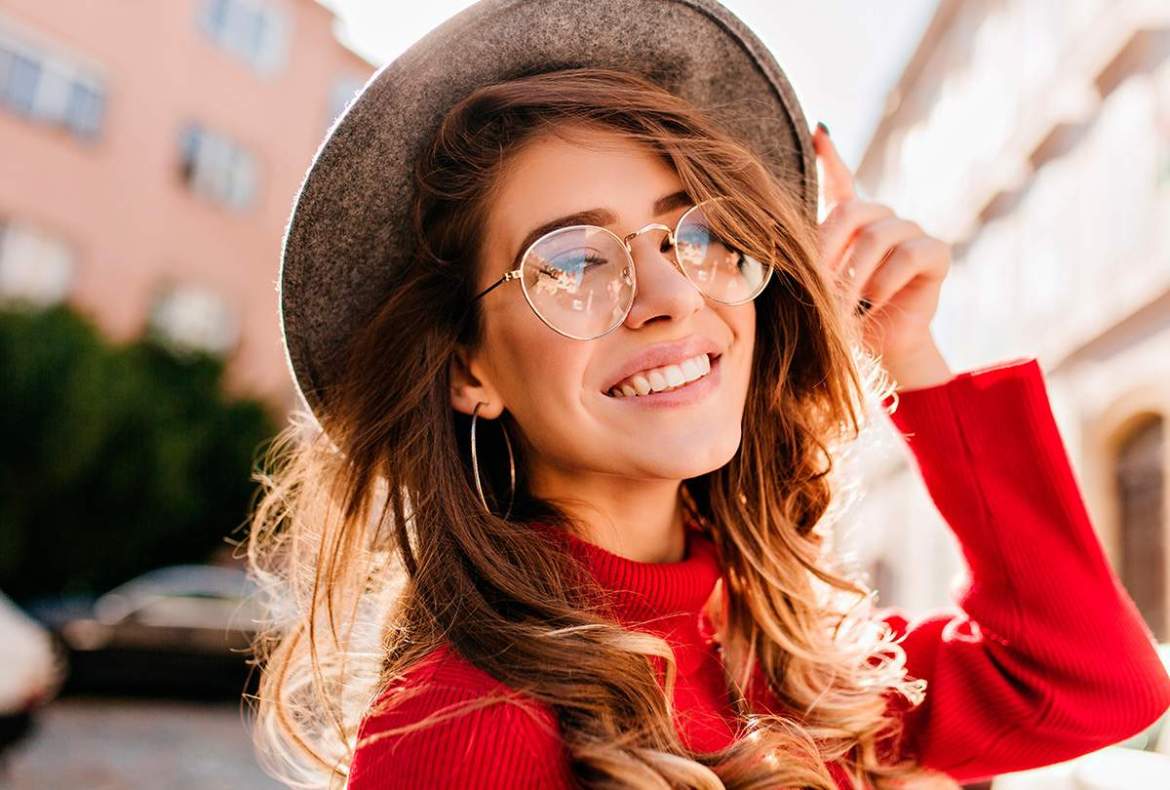 mulher sorrindo, de chapéu e blusa vermelha, com cabelo e mechas morena iluminada