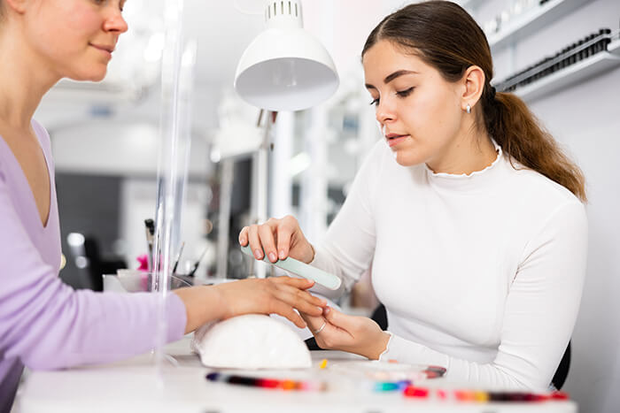nail designer lixando unha de cliente e utilizando os melhores produtos profissionais para salão de manicure