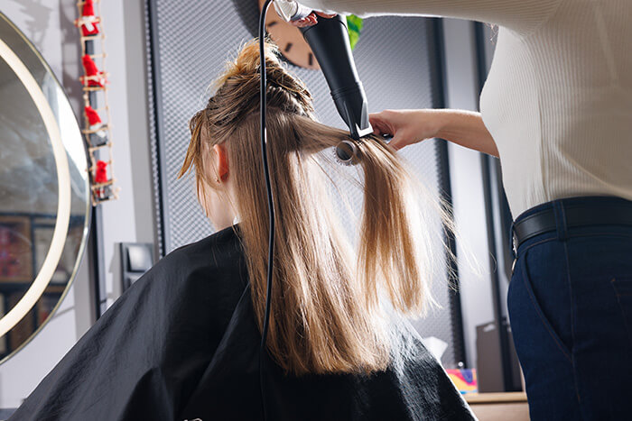 cabeleireira escovando e secando cabelo de cliente com os melhores produtos profissionais para salão