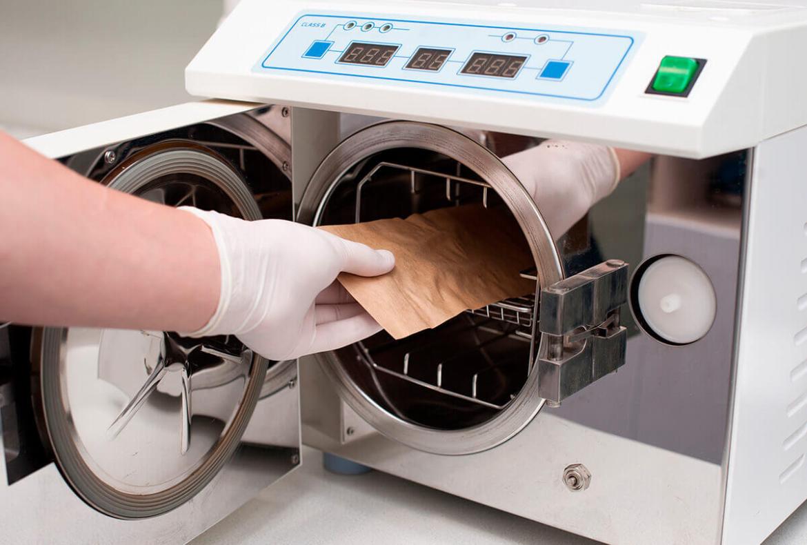 profissional de salão de beleza colocando envelope na autoclave para esterilização de materiais