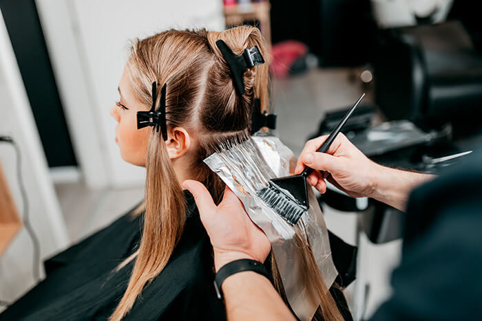 cabeleireiro fazendo mechas em cabelo loiro e usando papel-alumínio