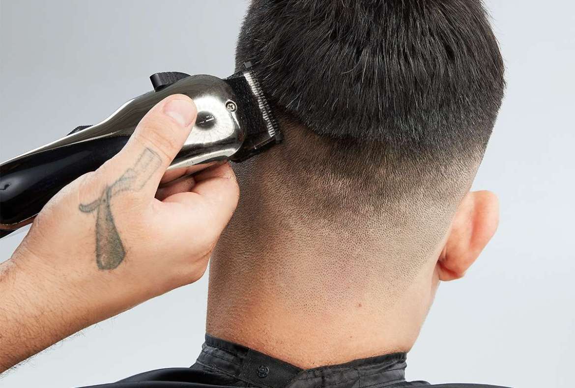cabeleireiro usando máquina de cortar cabelo em cliente masculino